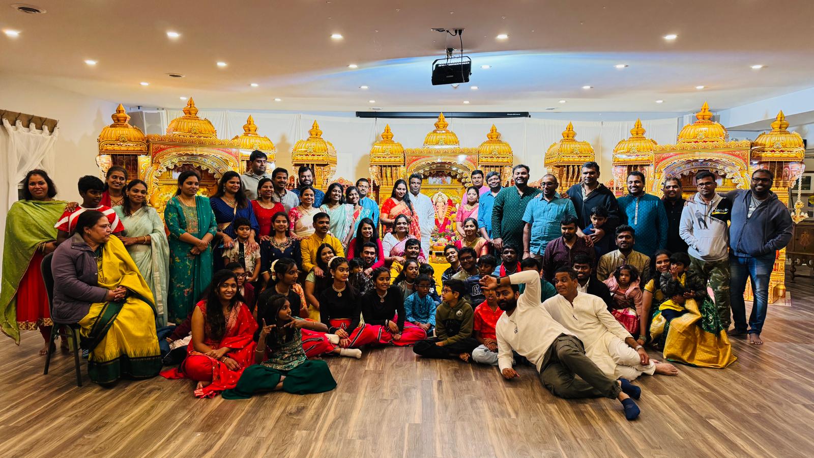 Large community group photo in front of the ornate golden mandap, 2025